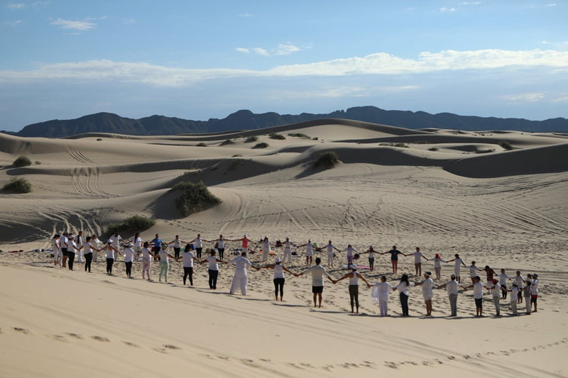 A circular gathering of yoga ehusiasts and a symbolic moveme for peace during a yoga eve in the dunes of Mexico