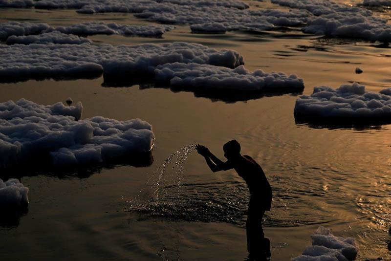 A man prays in the polluted, sedime-filled waters of the Yamuna River in New Delhi at sunrise; Photo source: the guardian; Photographer name: Sajjad Hussain