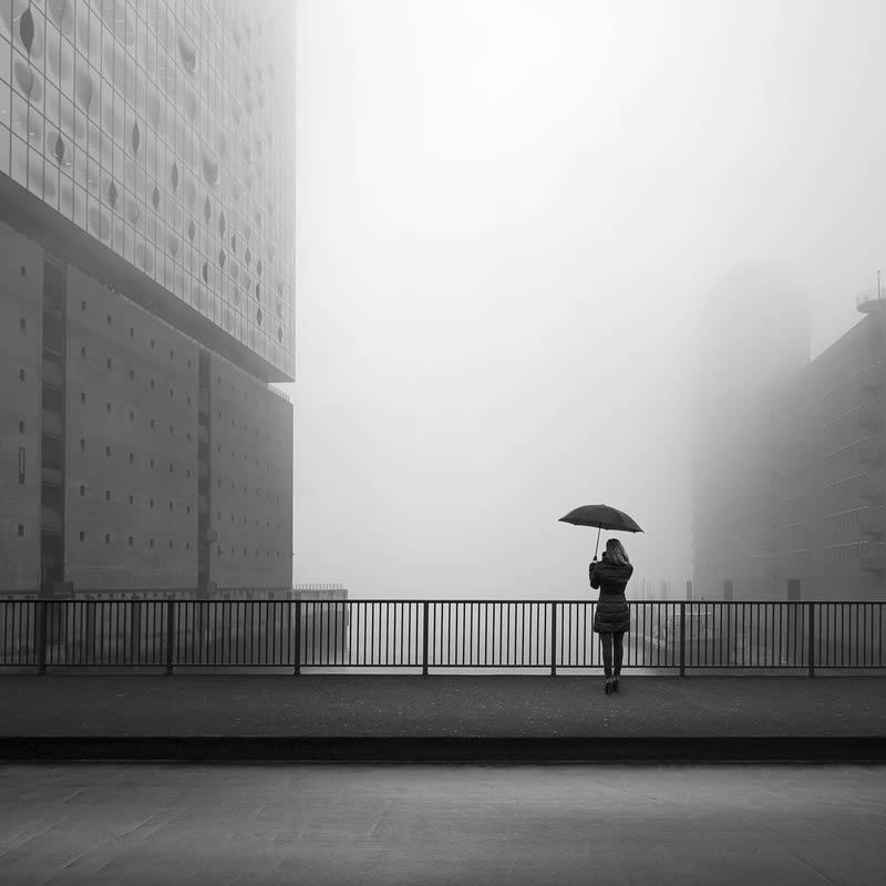 A person standing with an umbrella next to a metal bridge