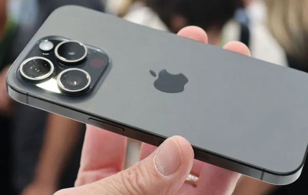 A close view of the flagship iPhone's triple camera module in the user's hand, with a matte design and Apple logo in the ceer of the back cover