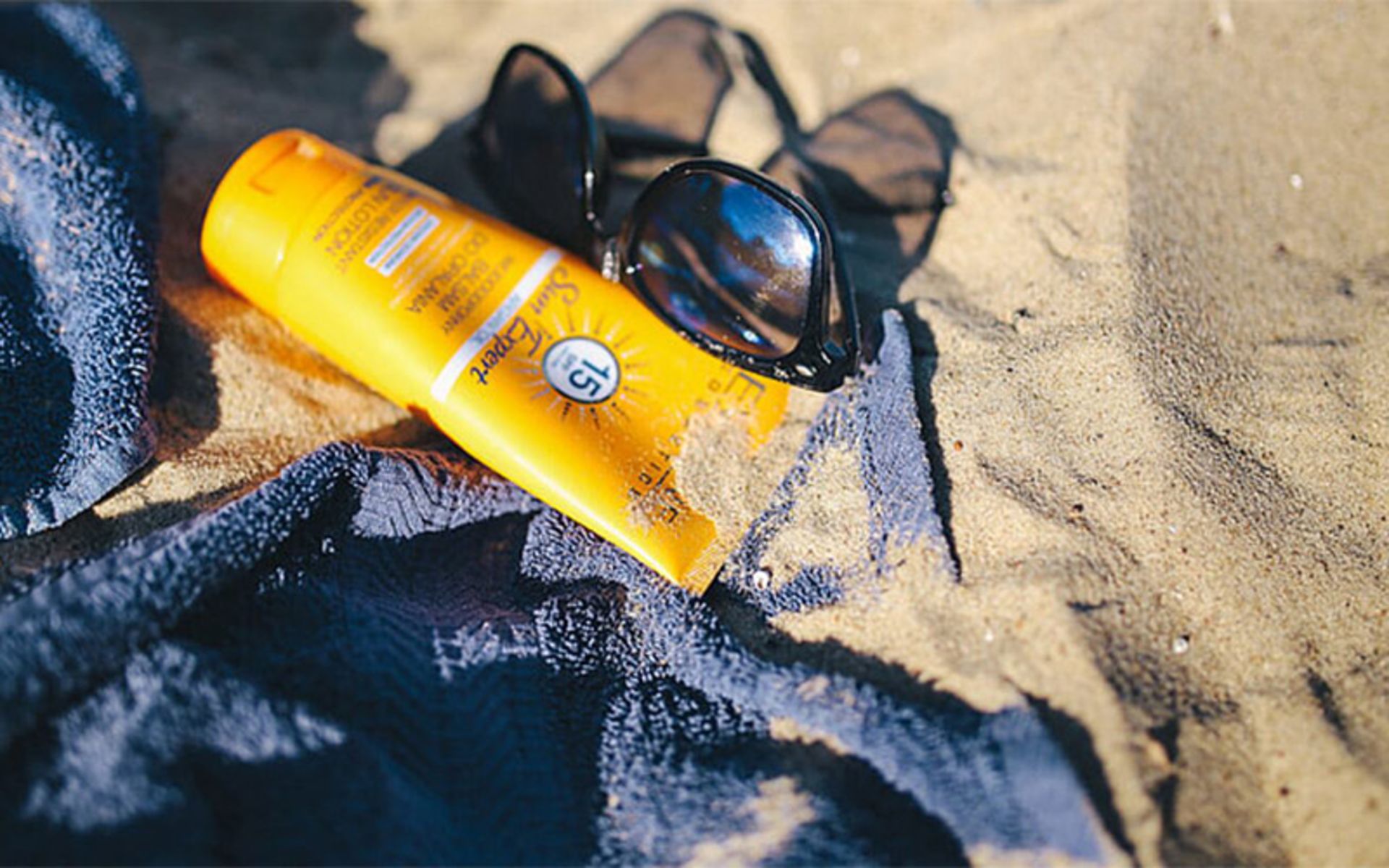 Mustard sunscreen with glasses and towels on the beach