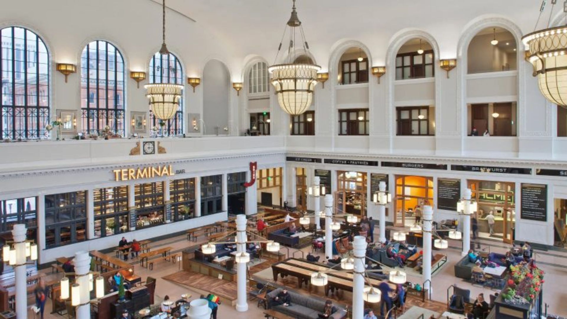 Chandeliers, chairs, windows and passengers in the white hall of Union Denver train station