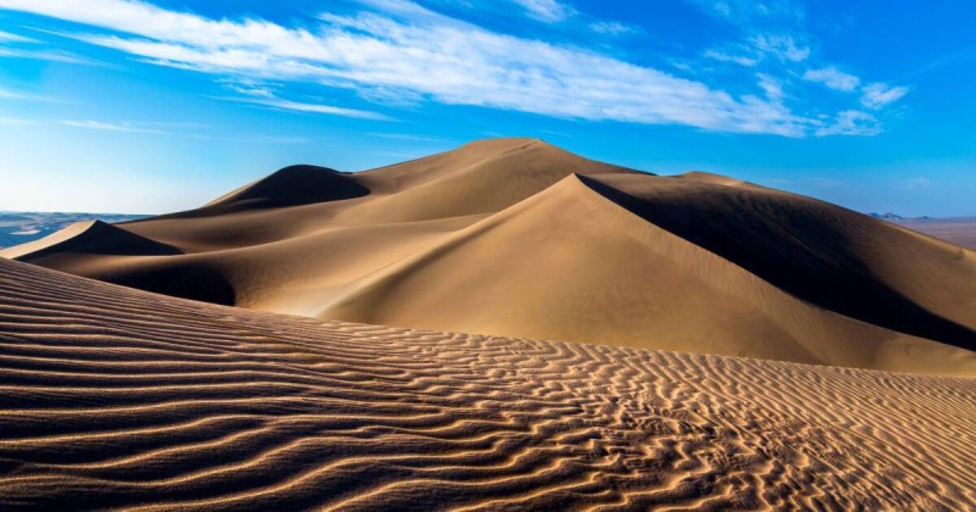 Smooth and wavy sand and blue sky with white clouds in the Lut Desert