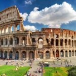 Colosseum amphitheater on sunny day, blue and cloudy sky, surrounding green space and visitors