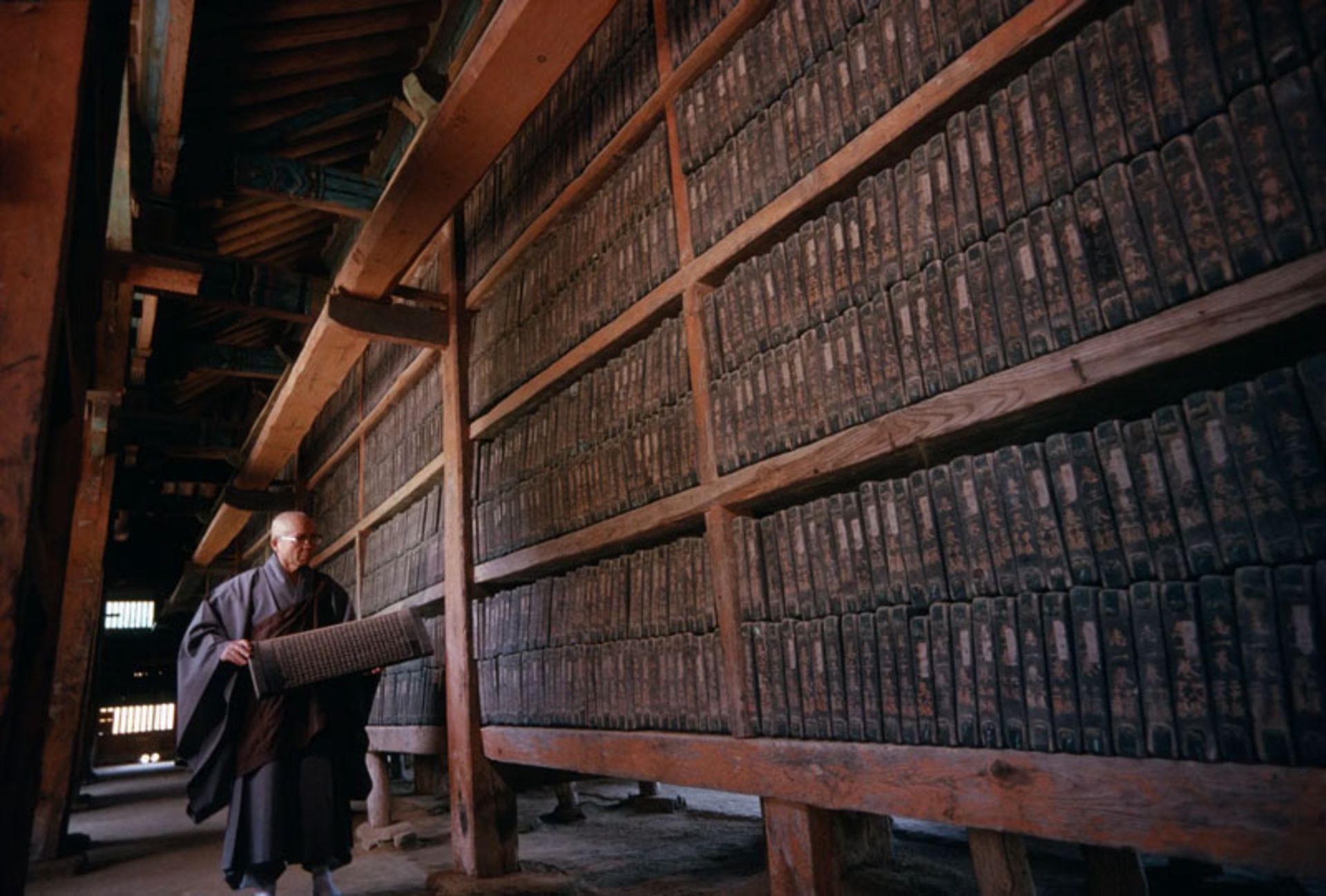 A Buddhist monk carrying a wooden block of the Koreana Tripitaka manuscript in the warehouses of Hyensa Temple in South Korea.