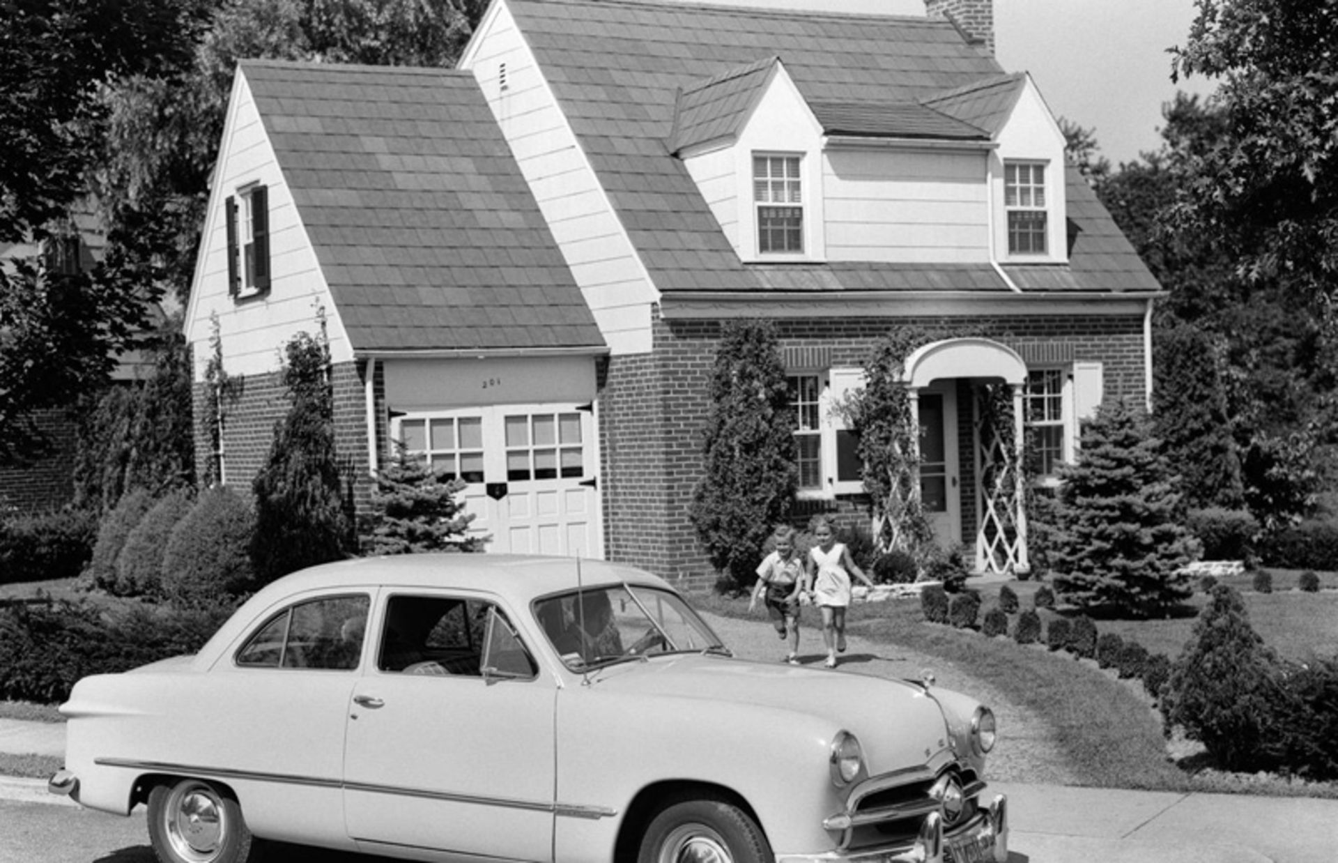 A classic car next to a house in the suburbs
