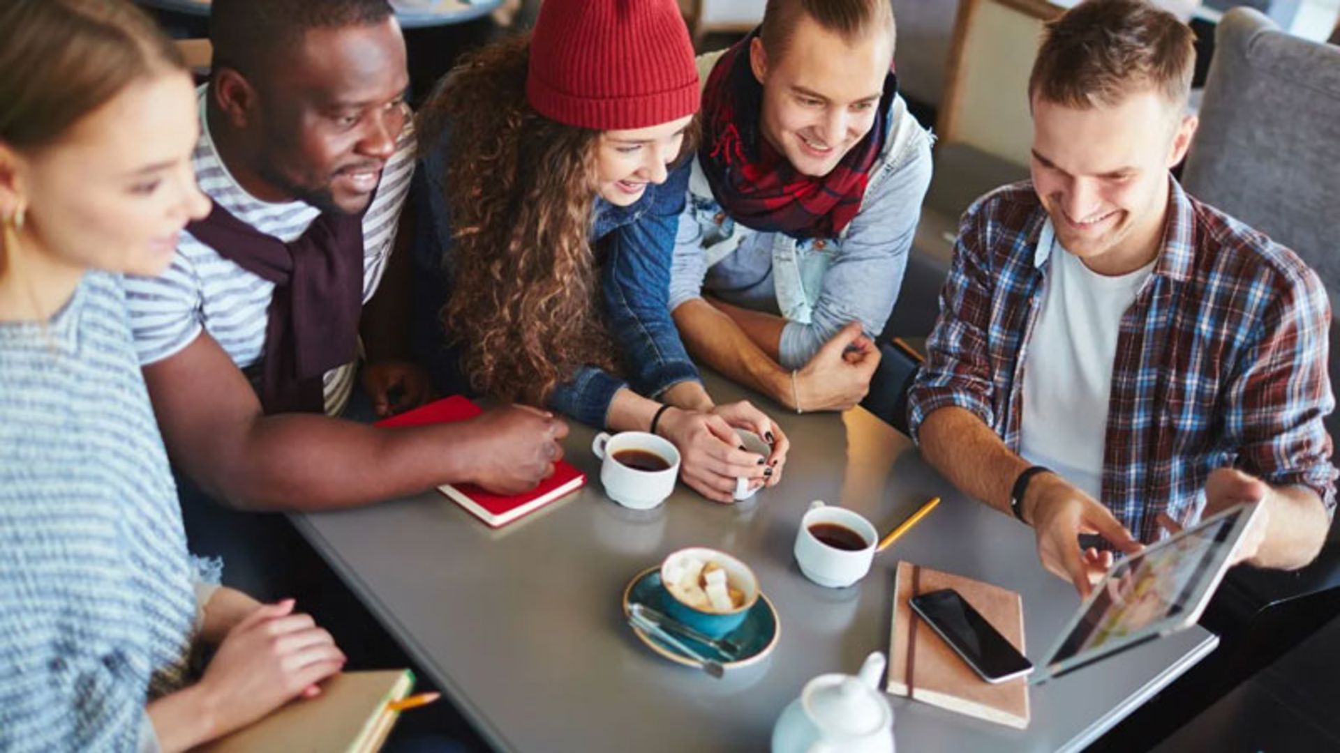 A group of young people in a cafe watching coe on a tablet