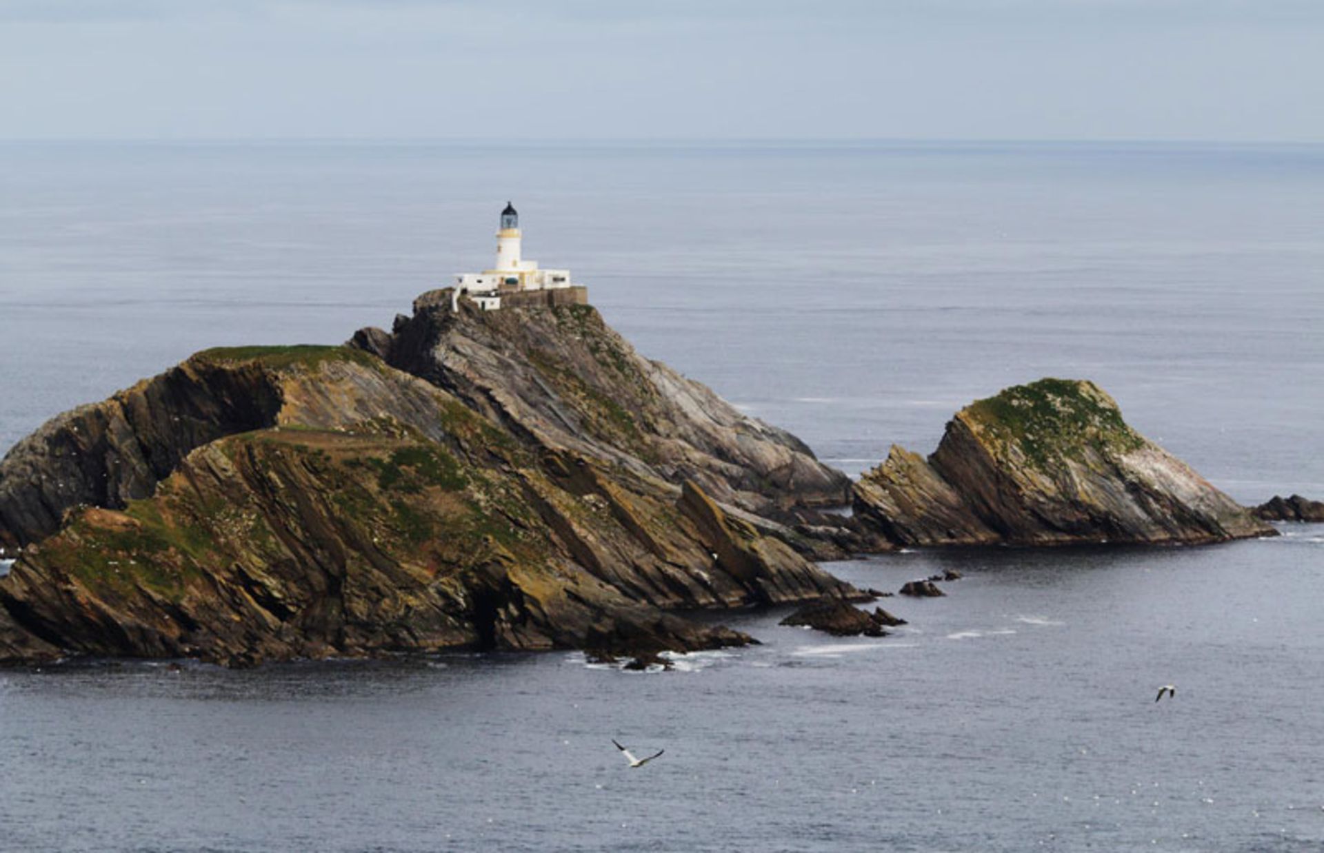 White lighthouse on top of sharp rocks in the middle of the sea