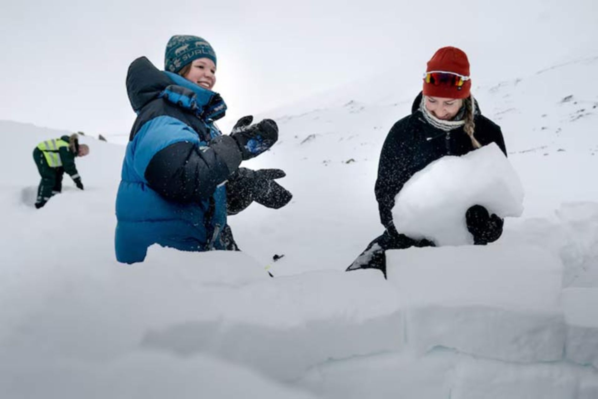 Two people in warm wier clothes building an ice house in the snow