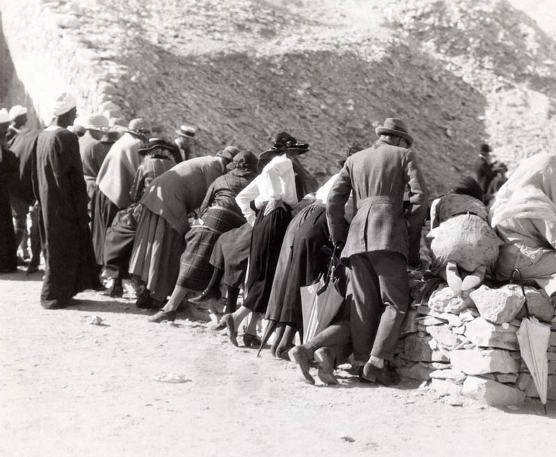  European visitors leaning over a rock ledge to look inside Tutankhamun's tomb