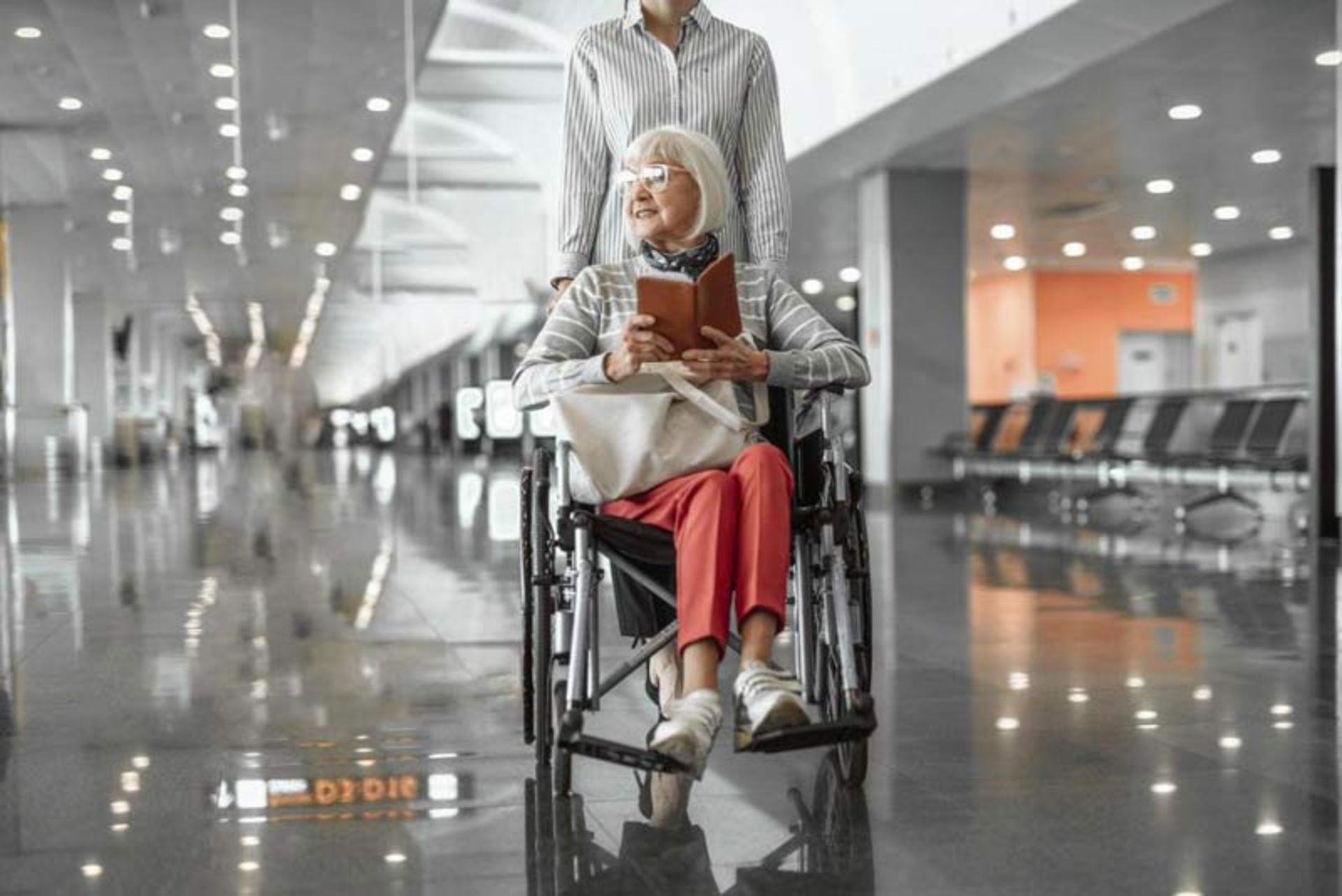 Elderly lady in wheelchair with travel documes in hand in modern terminal hall