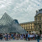 A close-up view of the glass pyramid of the Louvre Museum in Paris on a partly cloudy day