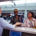 The smile of the airport attendant while handing over the documents and flight card to the passenger couple behind the counter